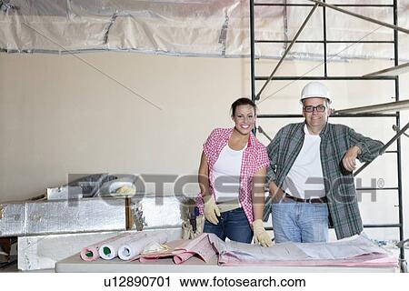 Stock Image - Portrait of happy team of architects with building plans at construction site. Fotosearch