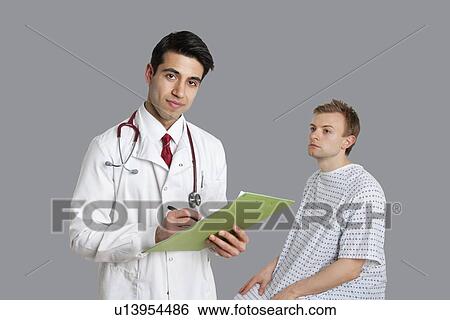 Stock Photograph - Portrait of Indian doctor writing on clipboard with patient sitting besides. Fotosearch