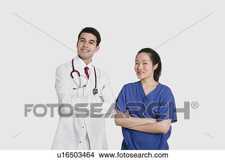 Picture - Portrait of male doctor and female nurse standing with hands folded over gray background. Fotosearch