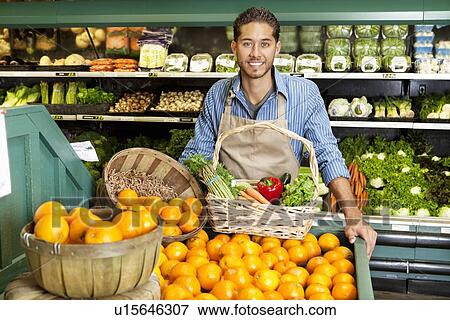 Stock Photo - Portrait of man in supermarket with vegetable basket standing near oranges stall. Fotosearch