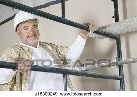 Stock Photo - Portrait of mature man climbing scaffold. Fotosearch