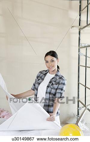 Stock Photo - Portrait of mid adult architect holding blueprints at construction site. Fotosearch