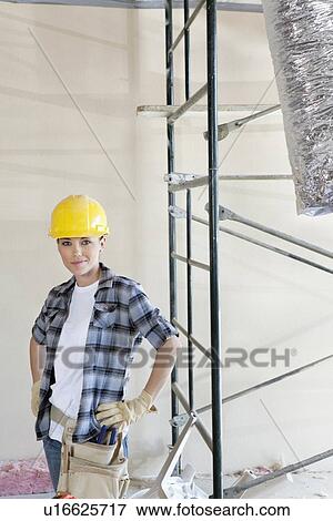Stock Photo - Portrait of mid adult woman standing with hands on hips at construction site. Fotosearch