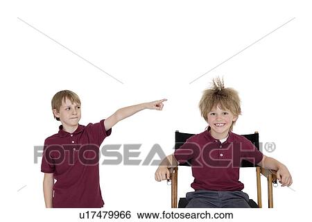 Stock Photograph - Portrait of school boy smiling while friend pointing at him over white background. Fotosearch