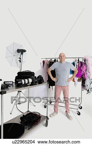 Portrait of senior man with hands on hips standing in front of clothes rack in studio View Large Photo Image Picture - Portrait of senior man with hands on hips standing in front of clothes rack in studio. Fotosearch