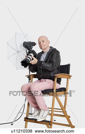 Portrait of senior photographer sitting on director's chair with camera View Large Photo Image Stock Photo - Portrait of senior photographer sitting on director's chair with camera. Fotosearch