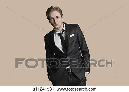 Stock Image - Portrait of young businessman with hands in pockets over colored background. Fotosearch