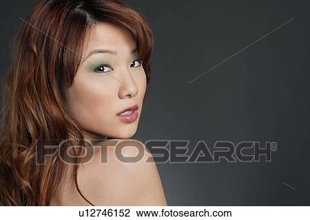 Stock Image - Portrait of young Chinese woman with eye shadow looking back over colored background. Fotosearch