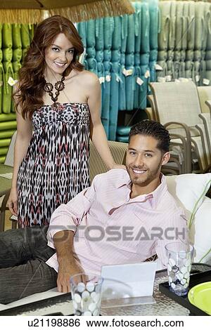 Stock Photograph - Portrait of young couple shopping for sofa in store. Fotosearch