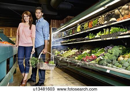 Portrait of young couple standing with vegetable basket in supermarket View Large Photo Image Stock Image - Portrait of young couple standing with vegetable basket in supermarket. Fotosearch