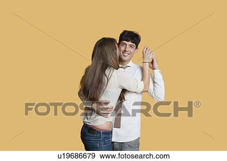 Stock Photo - Portrait of young man hugging girlfriend over colored background. Fotosearch
