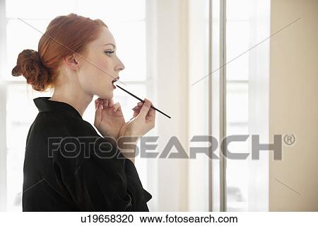 Profile view of a young woman in robe applying lip liner View Large Photo Image Stock Image - Profile view of a young woman in robe applying lip liner. Fotosearch