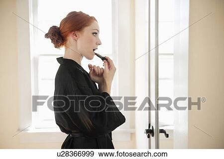 Profile view of a young woman in robe applying lipstick View Large Photo Image Stock Photo - Profile view of a young woman in robe applying lipstick. Fotosearch