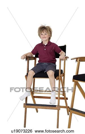 Stock Photograph - School kid sitting on director's chair over white background. Fotosearch