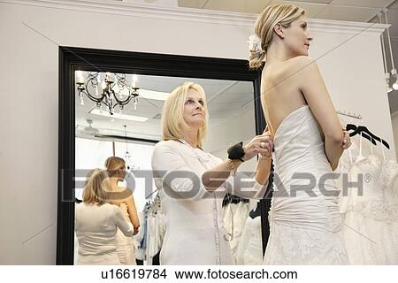 Senior owner assisting young bride getting dressed in wedding gown View Large Photo Image Picture - Senior owner assisting young bride getting dressed in wedding gown. Fotosearch