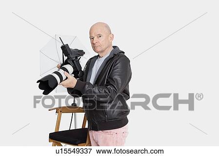 Senior photographer holding camera standing in studio View Large Photo Image Stock Photo - Senior photographer holding camera standing in studio. Fotosearch