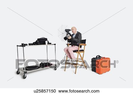 Stock Image - Senior photographer looking at camera while sitting on director's chair in studio. Fotosearch