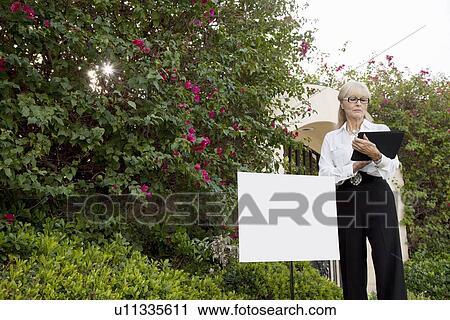 Senior real estate agent standing by sign board reading from clipboard View Large Photo Image Stock Image - Senior real estate agent standing by sign board reading from clipboard. Fotosearch