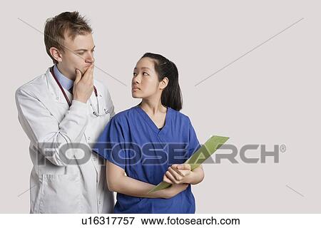 Serious Caucasian doctor and Asian nurse looking at each other over gray background View Large Photo Image Stock Photo - Serious Caucasian doctor and Asian nurse looking at each other over gray background. Fotosearch