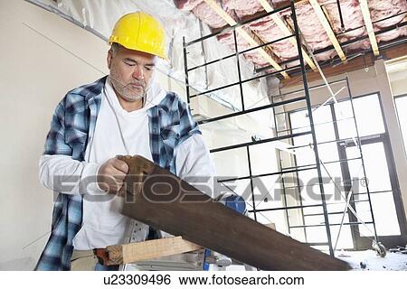 Stock Photograph - Serious male construction worker cutting wood with handsaw. Fotosearch