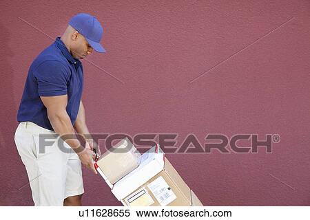 Stock Photography - Side view of muscular African American delivery man with handtruck. Fotosearch