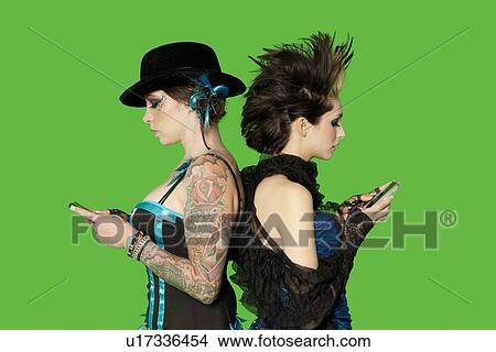 Picture - Side view of punk females standing back to back over with mobile phones over green background. Fotosearch