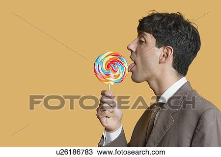 Side view of young businessman licking lollipop over colored background View Large Photo Image Stock Image - Side view of young businessman licking lollipop over colored background. Fotosearch
