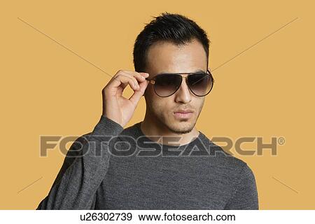 Stock Photo - Stylish young man wearing sunglasses over colored background. Fotosearch