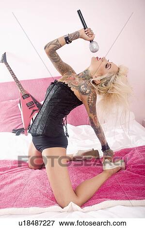 Stock Photo - Tattooed woman wearing corset singing in bed. Fotosearch