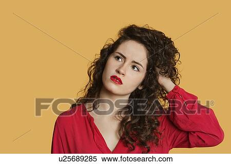Stock Photography - Thoughtful young woman with hand in hair over colored background. Fotosearch