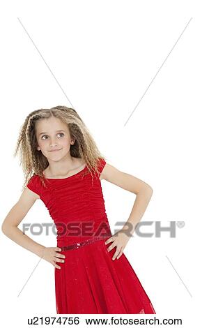 Stock Photograph - Tilt image of girl wearing red frock looking sideways with hands on hips over white background. Fotosearch