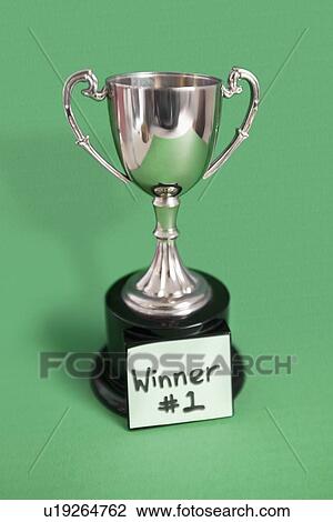 Stock Image - Trophy with sticky note for winner over colored background. Fotosearch