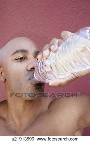 Stock Photo - Young African American man drinking water from bottle over colored background. Fotosearch