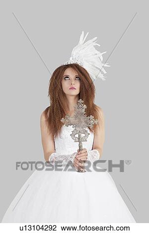 Young brunette bride in wedding gown holding crucifix while looking up over light gray background View Large Photo Image Stock Image - Young brunette bride in wedding gown holding crucifix while looking up over light gray background. Fotosearch