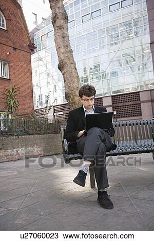 Young businessman working on laptop while sitting on bench View Large Photo Image Stock Image - Young businessman working on laptop while sitting on bench. Fotosearch
