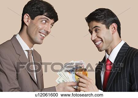 Stock Image - Young businessmen smiling while looking at each other with Euros in hand. Fotosearch