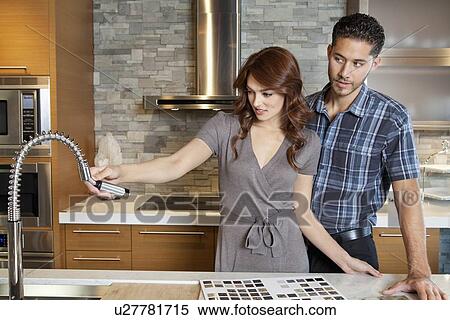 Stock Photography - Young couple looking at sink faucet on kitchen counter in model home. Fotosearch