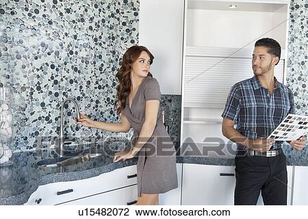 Stock Image - Young couple standing in model home kitchen while looking at each other. Fotosearch