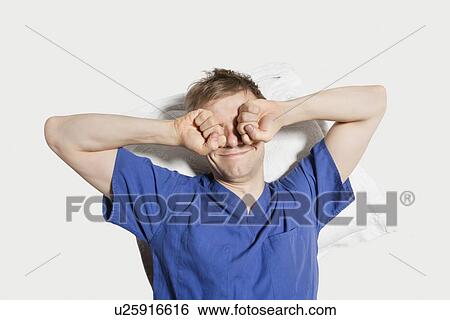 Stock Photograph - Young man rubbing eyes while waking up over colored background. Fotosearch