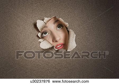 Stock Photograph - Young Middle eastern woman looking up from ripped paper hole. Fotosearch