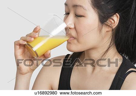Stock Image - Young woman drinking orange juice over gray background. Fotosearch