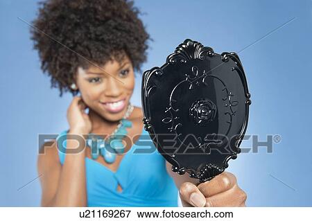 Young woman holding looking at mirror over colored background View Large Photo Image Stock Photo - Young woman holding looking at mirror over colored background. Fotosearch