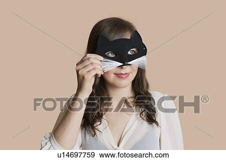 Young woman looking through eye mask over colored background View Large Photo Image Stock Photo - Young woman looking through eye mask over colored background. Fotosearch