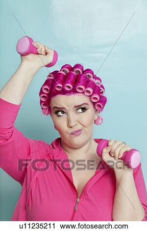 Young woman making face while lifting dumbbell over colored background View Large Photo Image Stock Image - Young woman making face while lifting dumbbell over colored background. Fotosearch