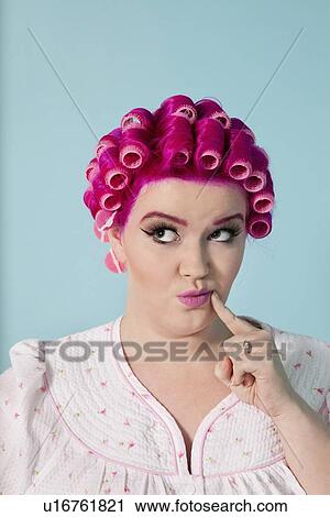Stock Image - Young woman with finger on cheek contemplating over colored background. Fotosearch