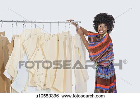 Stock Photograph - African American female designer with sewing patterns on clothes rack over gray background. Fotosearch