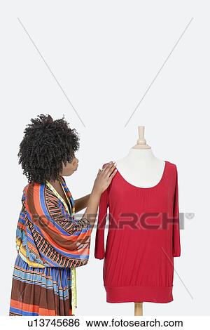 Stock Photograph - African American female fashion designer looking at red tunic over gray background. Fotosearch