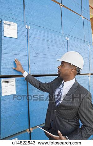 Stock Image - African American male contractor inspecting wooden planks while holding tablet PC. Fotosearch