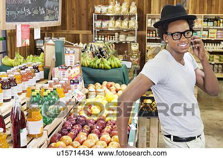 Picture - African American man using cellphone at supermarket. Fotosearch