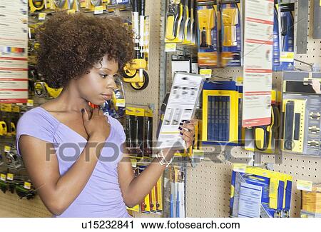 Stock Image - African American woman reading instructions on a product at super market. Fotosearch